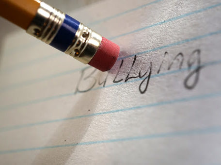 The word "bullying" being erased by a pencil eraser
