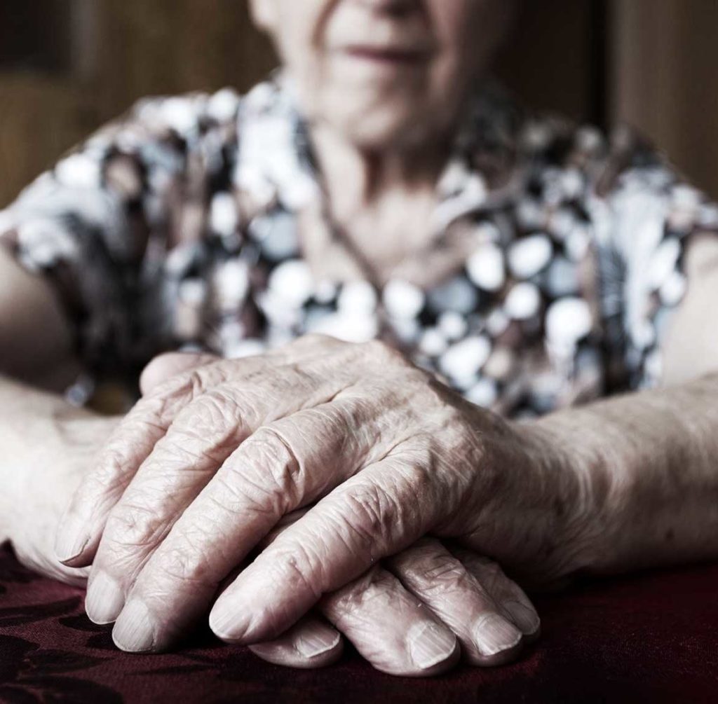 An elderly woman sitting with her wrinkled hands stacked in front of her