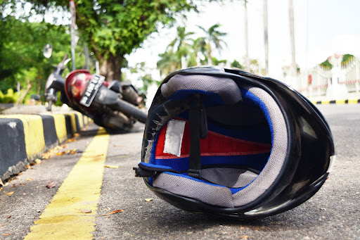 A motorcycle leaning against a curb with a motorcycle helmet resting on the pavement after an accident