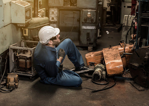 An employee at an industrial plant sitting on the floor in pain after a machinery accident