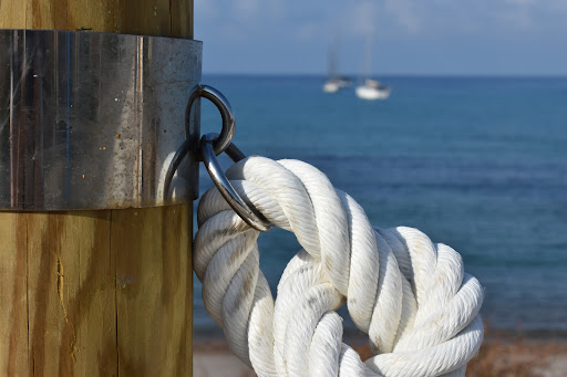 A thick white rope tied to a maritime mooring on a dock