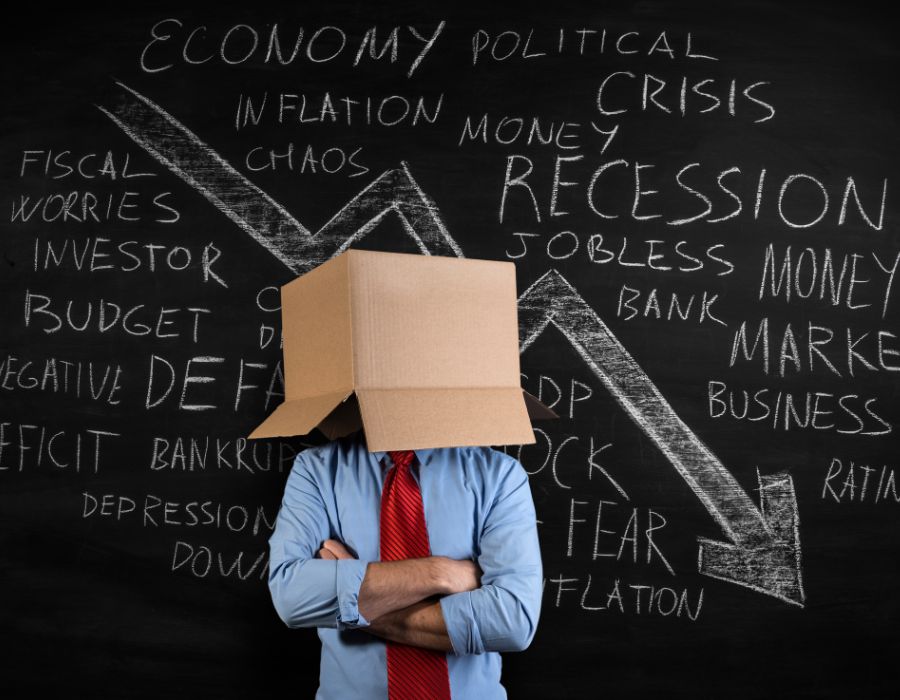 man covering face with cardboard box with a declining graph behind him