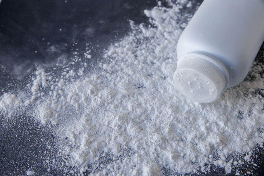A bottle of talcum powder, a product that can cause cancer, spilled on a black surface.