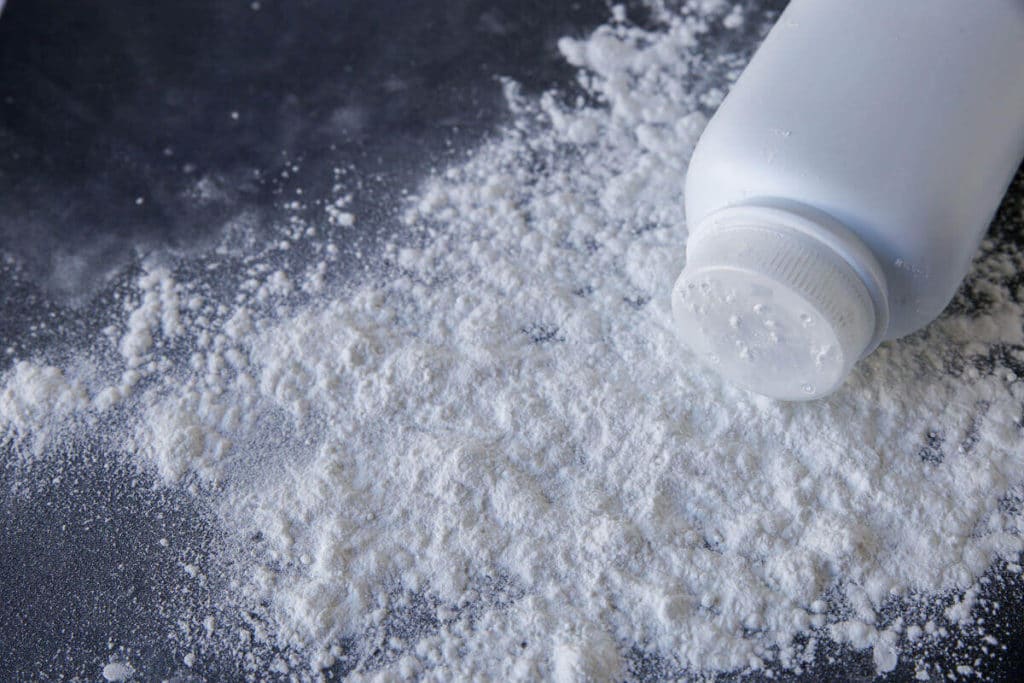 Talcum powder spilled out of a white bottle on a dark surface