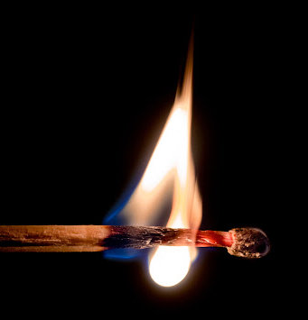 A flame burning on a matchstick against a black background.