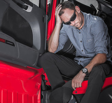 Fatigued truck driver sits in the cab of a big red truck with the door open