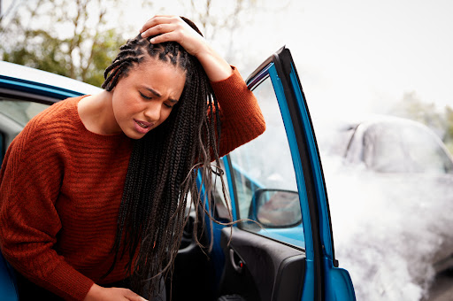 A young woman exiting a car and holding her head in pain after an accident with an underinsured motorist
