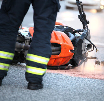 An emergency responder stands by a damaged motorcycle laying on the road after an accident in Denham Springs