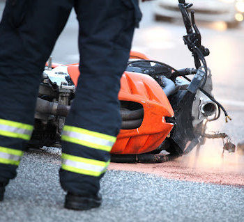 The legs of a firefighter standing in front of a damaged motorcycle laying in the street