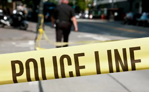 A police officer walks away from a yellow and black police line sectioning off the scene of a crime