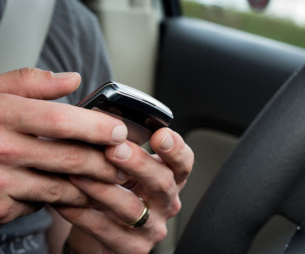 A closeup of a young man using both hands to text while driving
