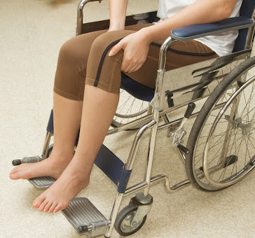 A paralyzed person in a wheelchair using their hands to reposition their legs.