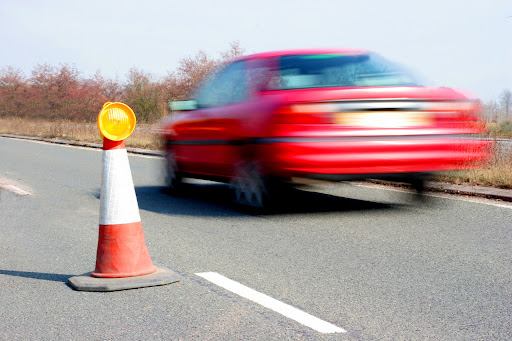 "a shot of a red car speeding on the highway,focus on traffic cone"