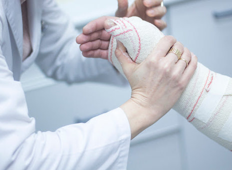 Médico aplicando una escayola y vendas en el antebrazo y la muñeca de un paciente para inmovilizarlo tras una lesión por fractura.