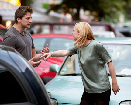 A man and a woman arguing in front of their vehicles after a car crash