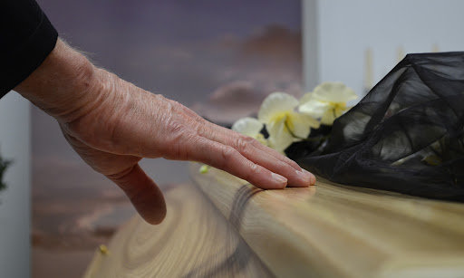 An older person's hand touching a casket at the funeral of a victim of wrongful death in Shreveport.