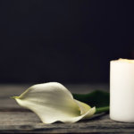 Burning candle and white calla on dark background with copy space. Sympathy card