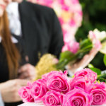 Mourning man and woman on funeral with pink rose standing at casket or coffin