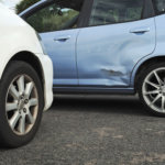 Blue and white cars stopped in light accident so door of blue car is bent, the paint is scratched and needs repair