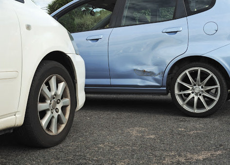 Blue and white cars stopped in light accident so door of blue car is bent, the paint is scratched and needs repair