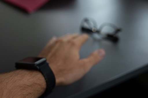 Blurred image of a man reaching for his glasses on a table.