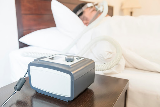 A man sleeps in the background wearing a CPAP mask, with the machine in the foreground.