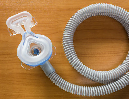 The mask and hose of a CPAP machine, a defective product that has been recalled, on a wooden table.