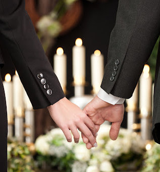 Two mourners gently hold hands at the funeral of a lost loved one.