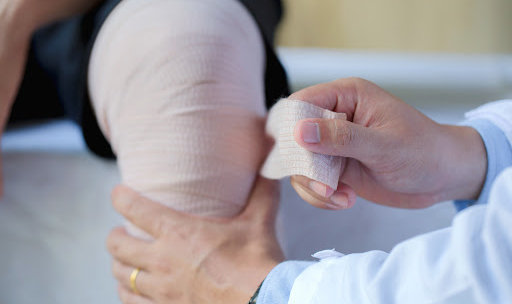 A doctor bandages a patient's knee after checking for infection after surgery.