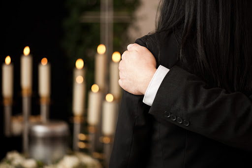 One person's hand on another's shoulder at the funeral for a victim of wrongful death.