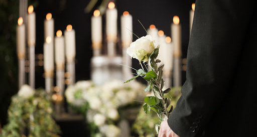 A man holds a white rose at the funeral of someone close to him.