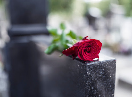 A single red rose on a black granite headstone.