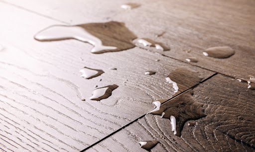 A puddle of liquid on a wood floor, a potential slipping hazard