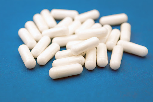 A pile of white capsule pills, similar to Elmiron, on a blue surface.