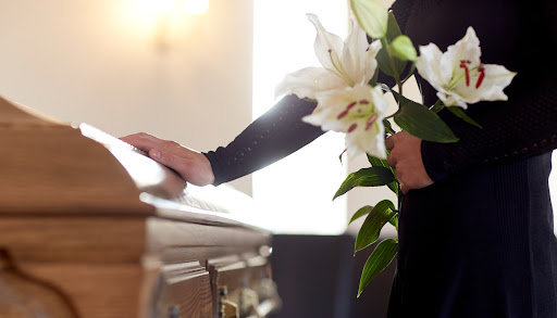 A woman holds a bunch of white lilies and touches a casket after the loss of a loved one.