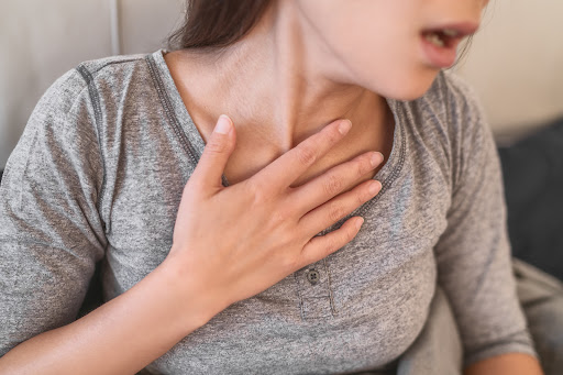 A young woman holding her hand to her chest while experiencing difficulty breathing.