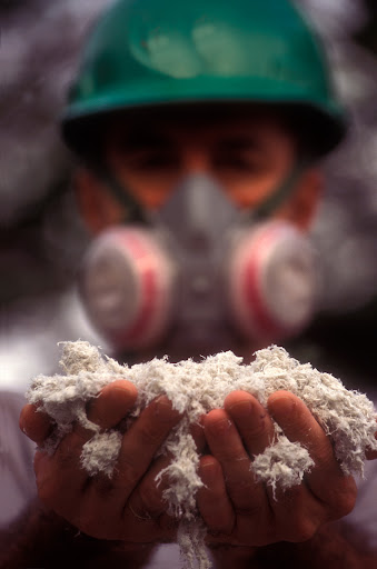 A worker in an industrial gas mask holds a pile of loose, but still hazardous, asbestos fibers.