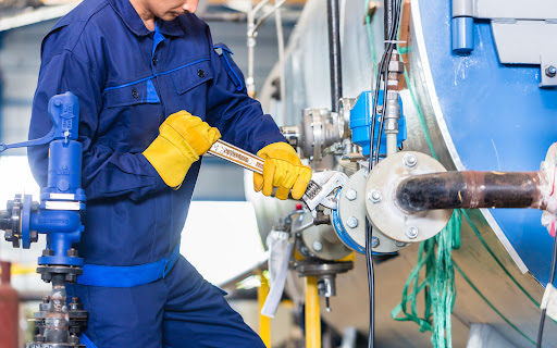 An industrial worker uses a wrench while performing maintenance on machinery