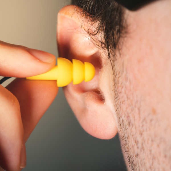 A man putting a yellow earplug into his ear.