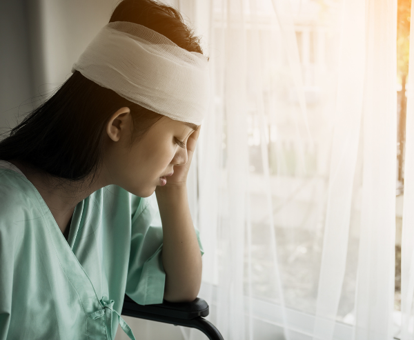 A woman with head bandages looking out the window in pain