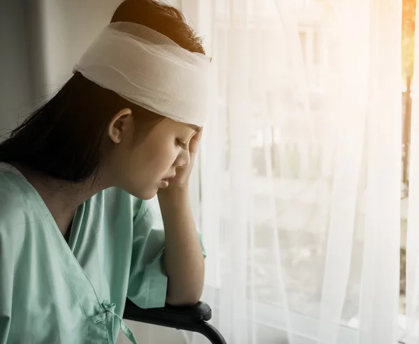 A woman with head bandages looking out the window in pain