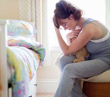 A mother holds her head and a teddy bear, grieving the wrongful death of a child.