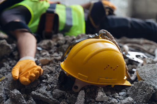 An injured worker lays in some rubble next to their hard hat after an accident