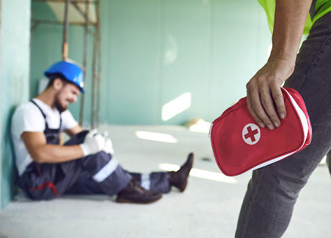 A worker bringing a first-aid kit to another worker with an injured leg