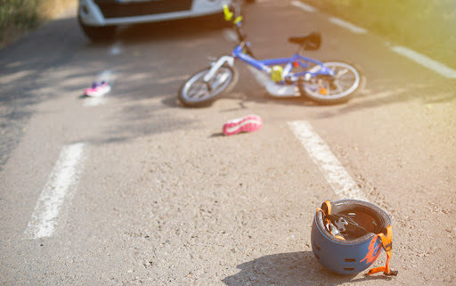 A child's bicycle and helmet on the road after an accident with a car in the background