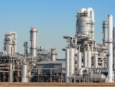 An industrial oil plant with silver tanks and pipes gleaming in the bright sun