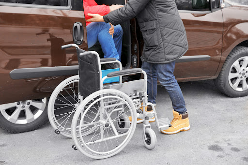 A helper assists a victim of catastrophic injuries get out of a vehicle and into a wheelchair