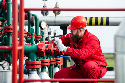 A worker in a red jumpsuit works on machinery at a refinery.