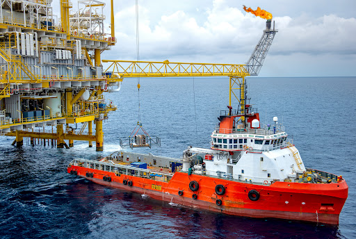 An orange and white ship docked with an offshore platform