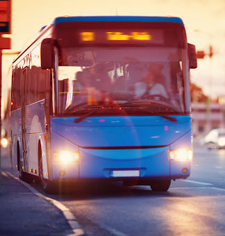 A blue bus driving through a Louisiana city at dusk